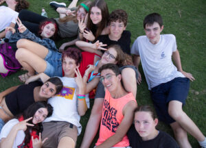 קבוצת חניכים ומדריכים יושבים על הדשא במחנה קיץ